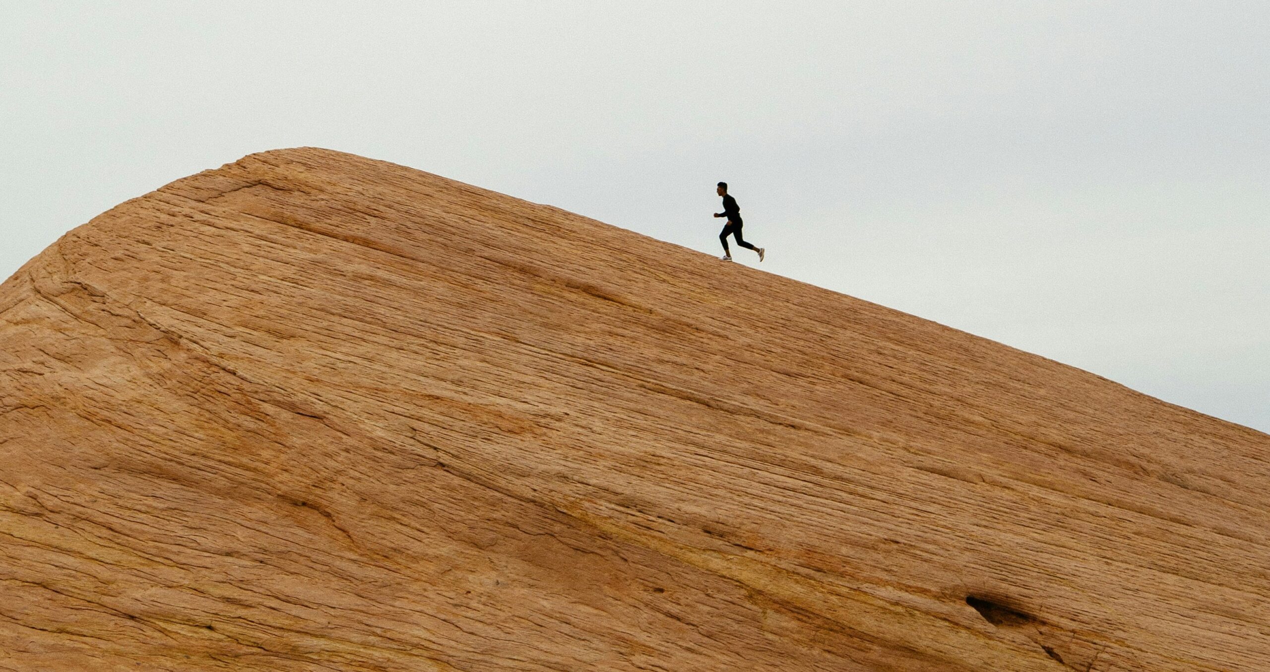 a person running up a hill with a grey and blue sky in the background representing something hard to do